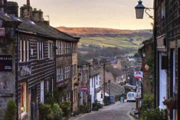 Picturesque countryside village near Manchester with stone cottages, rolling green hills, and a quiet scenic road surrounded by natural beauty.