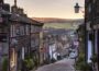 Picturesque countryside village near Manchester with stone cottages, rolling green hills, and a quiet scenic road surrounded by natural beauty.